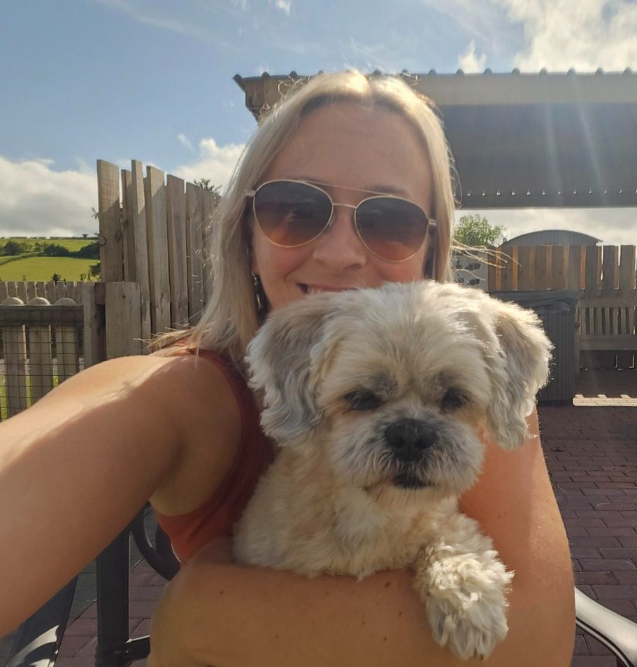 A woman wearing sunglasses holds a small dog outdoors.